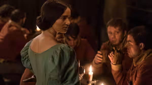 Clare (Aisling Franciosi) turns toward soldiers gathered around a candlelit table