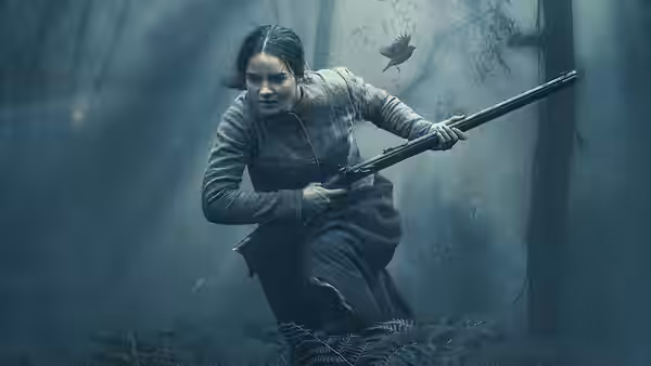Clare (Aisling Franciosi) runs through the woods carrying a rifle
