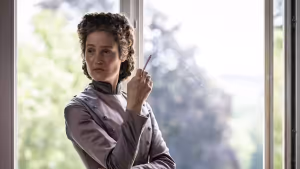Empress Elisabeth (Vicky Krieps) stands by a window holding a slender object