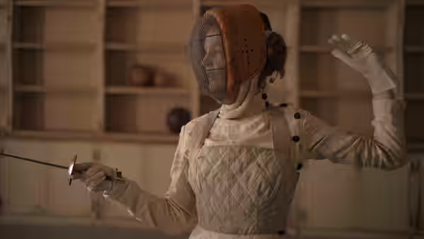 Empress Elisabeth (Vicky Krieps) wears fencing gear and raises her gloved hand, foil in hand