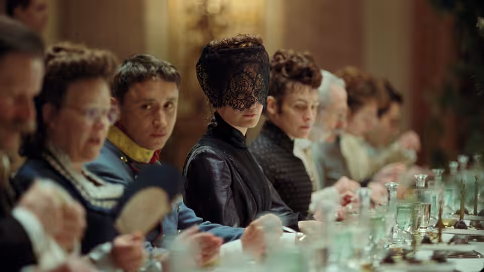 Empress Elisabeth (Vicky Krieps) sits veiled at a formal dining table among guests