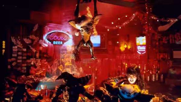 A gremlin hangs from the ceiling above a woman in a bar