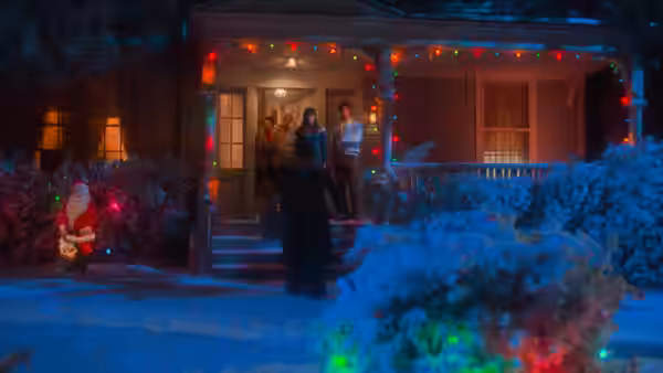 People stand on the porch of a house with Christmas lights at night