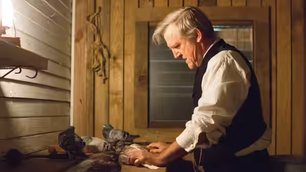 Andrew Borden (Jamey Sheridan) leans over a body in a wood-paneled room