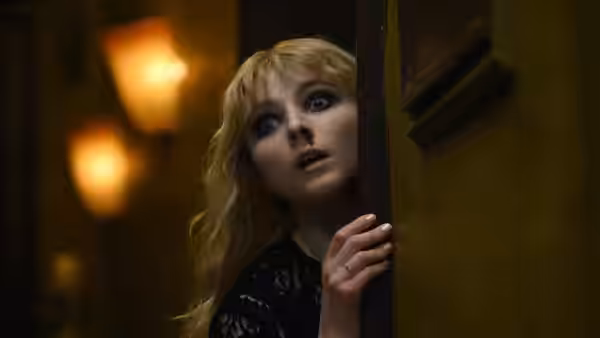 Sandie (Anya Taylor-Joy) peering from behind a wooden door with wide eyes