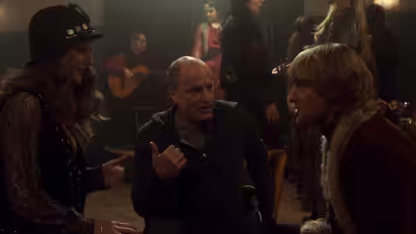 Woody Harrelson gesturing while speaking to Owen Wilson beside a woman in a bar