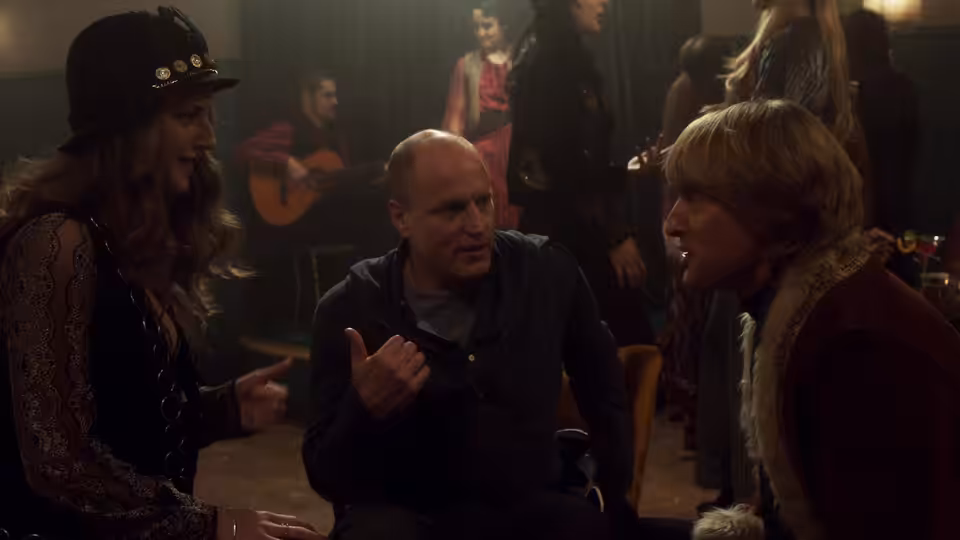 Woody Harrelson gesturing while speaking to Owen Wilson beside a woman in a bar
