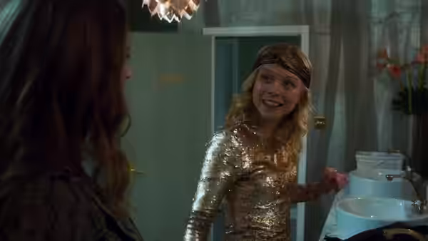 A young girl in gold smiling at a woman inside a bathroom