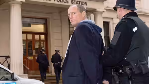 Woody Harrelson escorted by a police officer outside a station building
