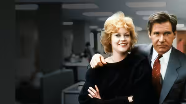 Tess McGill (Melanie Griffith) smiles beside Jack Trainer (Harrison Ford) in an office