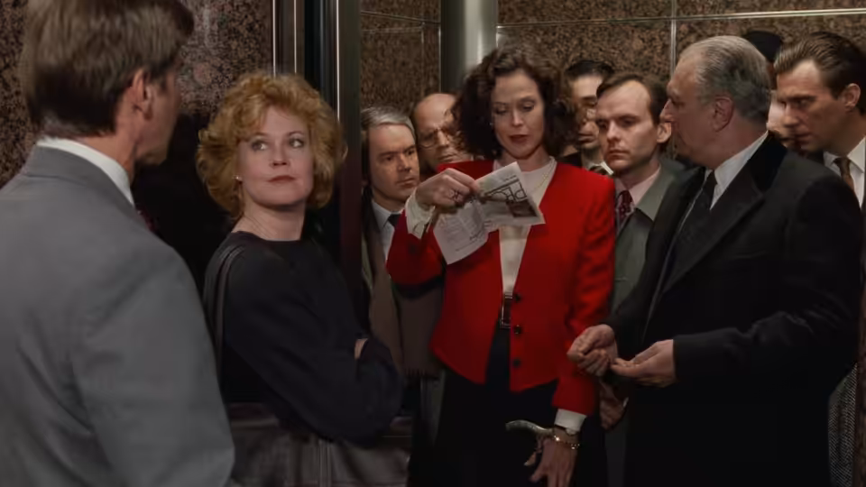 Katharine Parker (Sigourney Weaver) points to a newspaper in an elevator as Tess McGill (Melanie Griffith) watches