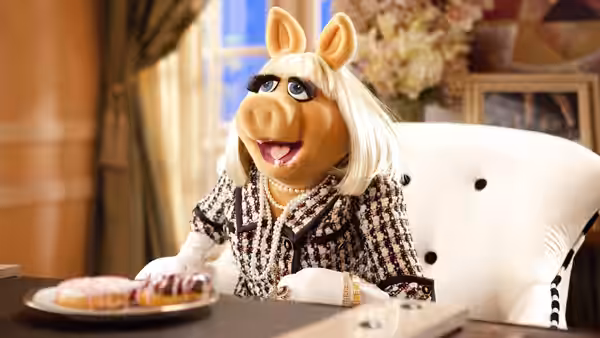 Miss Piggy (Eric Jacobson) sits at a table beside a plate of pastries