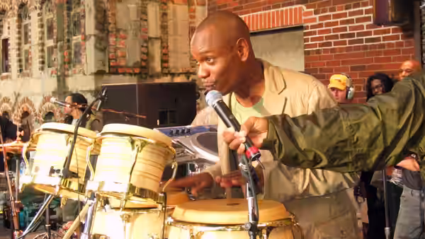 A musician playing conga drums while singing into a microphone outdoors