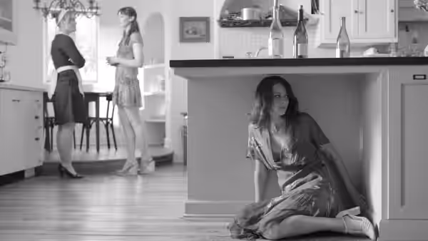 Beatrice (Amy Acker) seated on the floor beneath a kitchen counter