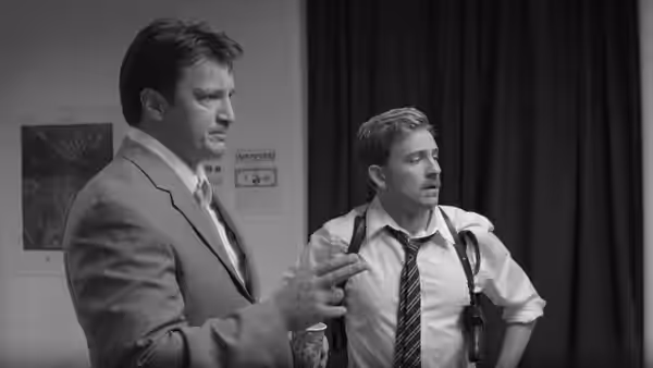 Two men in suits and ties standing together indoors near a poster