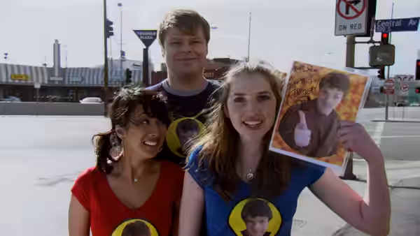 Three people holding a Dr. Horrible poster on a city street