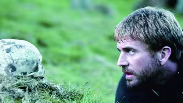 Hamlet (Mel Gibson) studies a skull lying in the grass