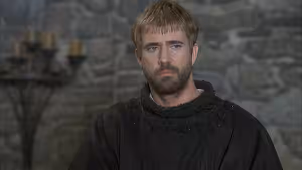 Hamlet (Mel Gibson) stands in dark clothing before a stone wall