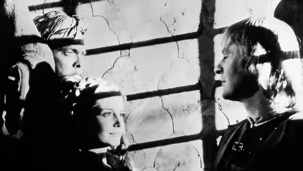 A woman and two men stand close together beside a cracked window