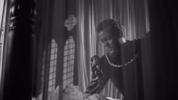 Othello (Orson Welles) leans over a bed in a shadowed chamber