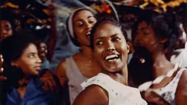 A man in a white shirt dances among women at a crowded gathering