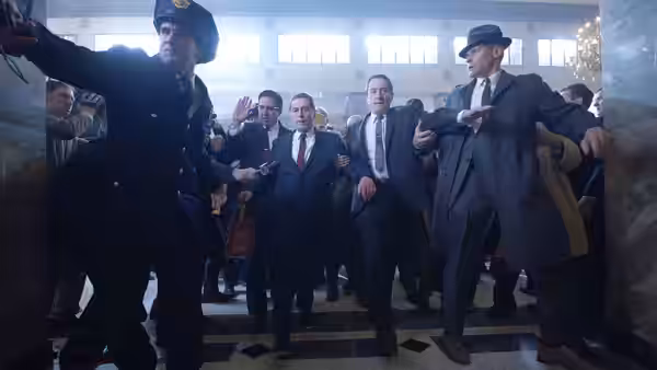 Police officer leading a group of men in suits through a hall