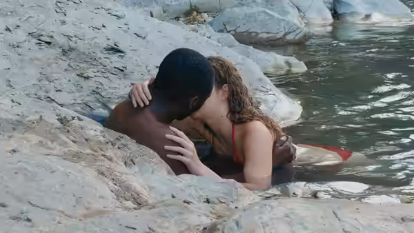 A couple kisses while embracing on rocks in shallow water