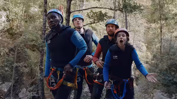 Four people in climbing gear pose together in a wooded area