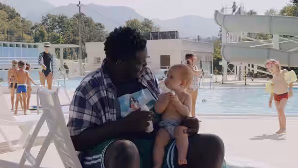 A man holds a baby on his lap by a swimming pool