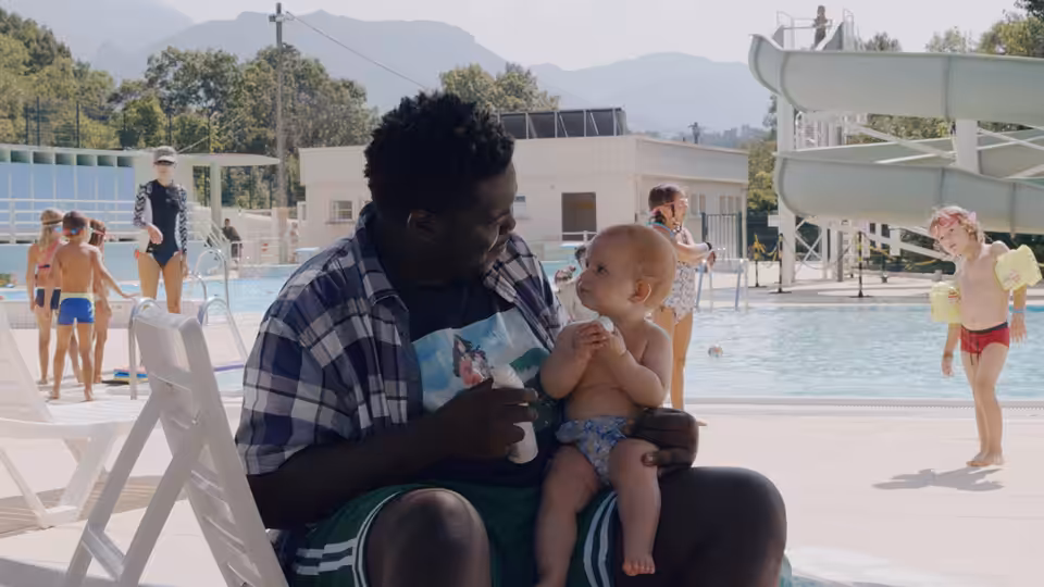 A man holds a baby on his lap by a swimming pool
