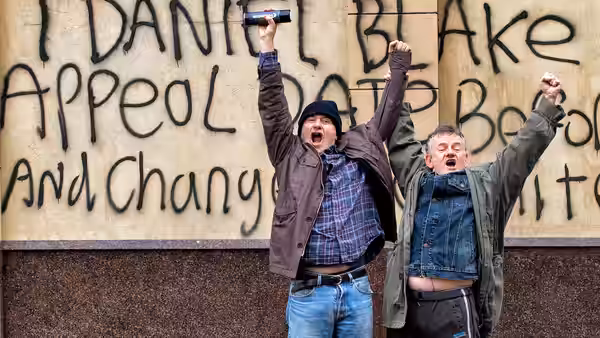 Dan (Dave Johns) and a companion raising their fists before a graffiti wall