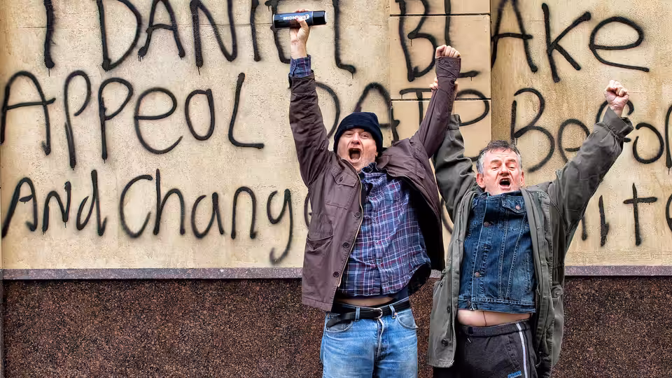 Dan (Dave Johns) and a companion raising their fists before a graffiti wall