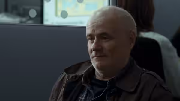 A middle-aged man with short gray hair sitting indoors and looking aside