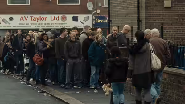 A long queue of people waiting outside a brick building on the street