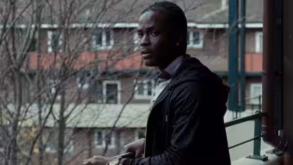 China (Kema Sikazwe) standing on a balcony holding a phone