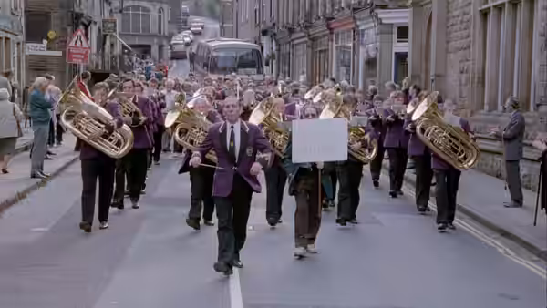 A brass band in purple jackets marching through a town street