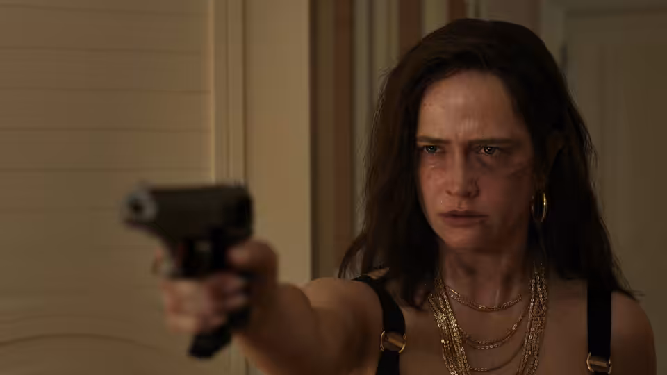 Nora Wolfe (Eva Green) pointing a pistol forward with a bruised face
