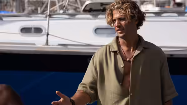 A man with curly blond hair gesturing on a boat