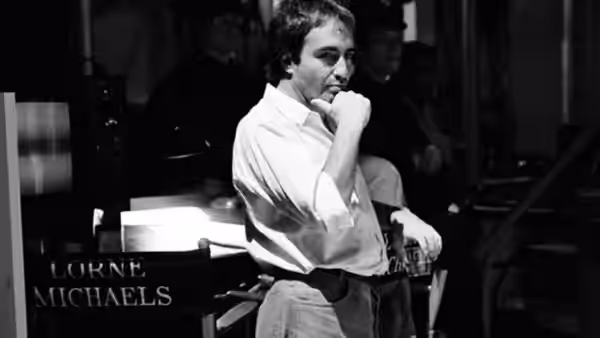 Lorne Michaels seated in his director's chair with hand to chin
