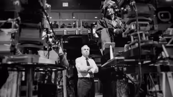 Man in white shirt and tie stands with arms crossed in studio