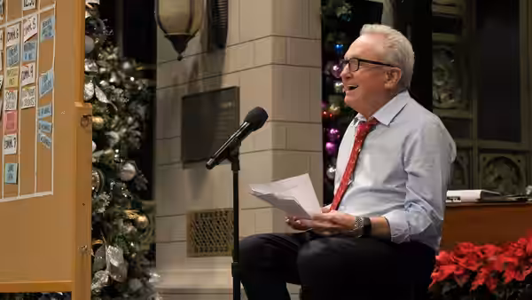 Lorne Michaels seated with papers beside a microphone and decorated Christmas tree