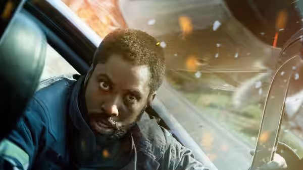 Protagonist (John David Washington) looking back during a fiery car chase