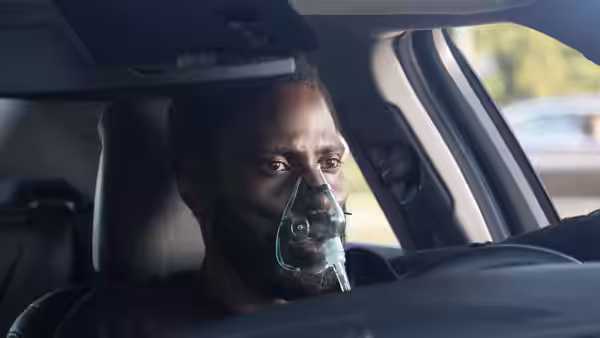 Protagonist (John David Washington) wearing an oxygen mask inside a car