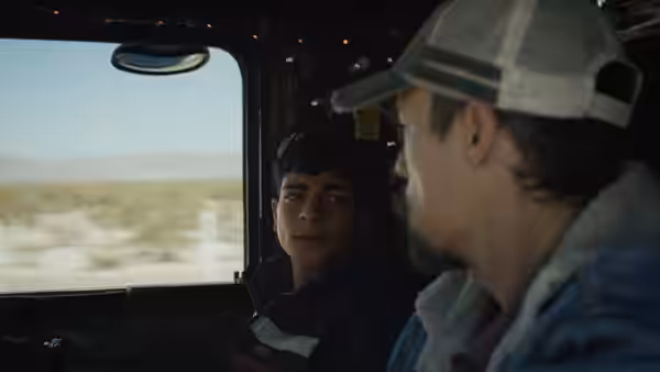 Two men sit inside a vehicle looking at each other in the desert
