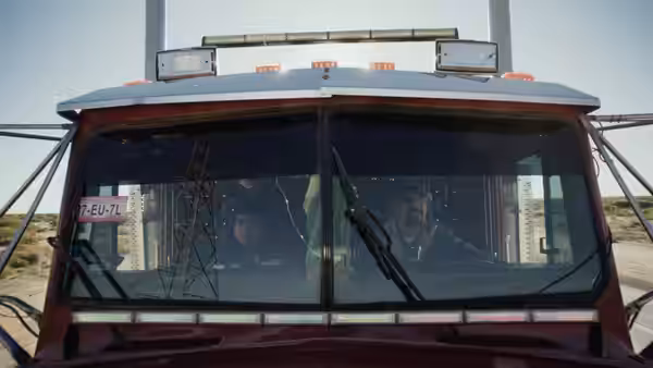 Two men inside the cab of a red truck in the desert