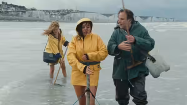 Three people in raincoats standing on a wet beach near white cliffs