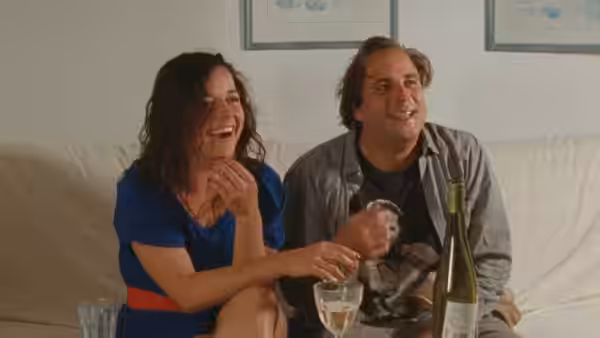 Patricia (Laure Calamy) laughing on the sofa beside Sylvain (Vincent Macaigne)