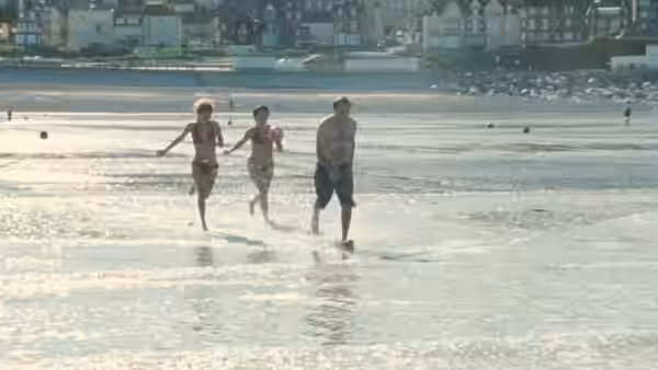 Three people running through shallow water along the shoreline