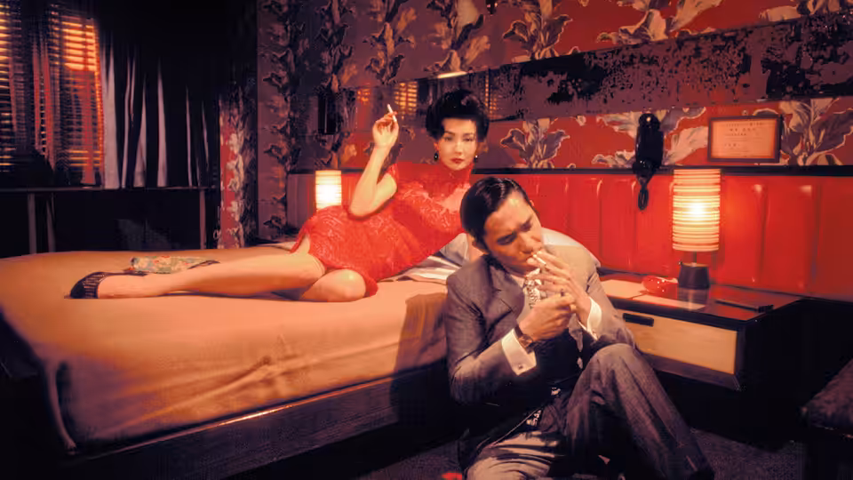 Su Li-zhen (Maggie Cheung) reclines on a bed while Chow Mo-wan (Tony Leung) smokes on the floor