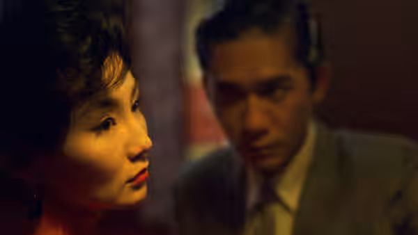 Su Li-zhen (Maggie Cheung) gazes aside as Chow Mo-wan (Tony Leung) looks downward